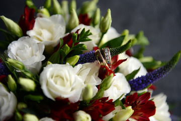 Two wedding rings on a wedding bouquet of white roses, close-up.