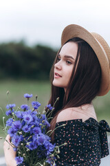 Beautiful brunette woman natural face in hat on the road with blue flowers