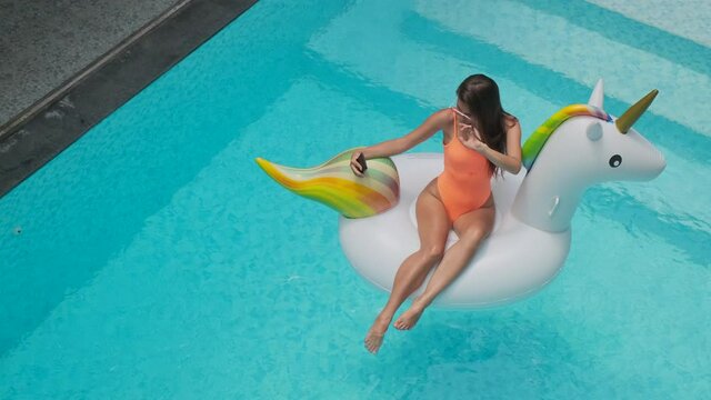 woman is photographing and floating on inflatable unicorn in pool
