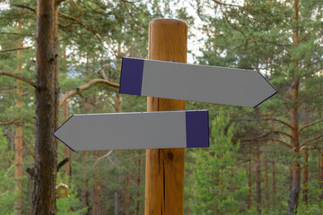 Two direction indicators on a wooden post. Background - green forest. Place for your text. Road fork concept.
