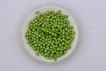 Green Peas. Green background. Peas background. Top view.Green pea in bowl on white background copy space. Fresh organic green peas on a round white plate. Vegetable harvesting