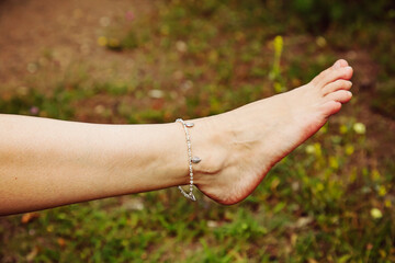 Female leg barefoot with fashionable boho anklet on the grass background