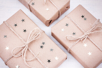 Three gifts wrapped in craft paper, decorated with asterisks and bandaged with jute rope. Close up.