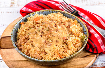 A bowl of satay chicken with fried rice on a wooden board and red napkin