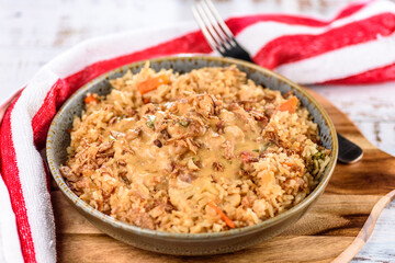 A bowl of satay chicken with fried rice on a wooden board and red napkin