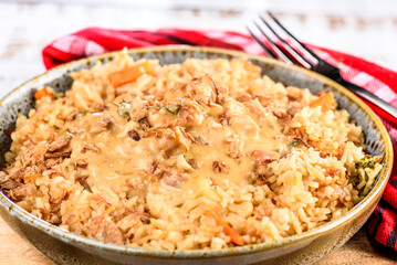 A bowl of satay chicken with fried rice on a wooden board and red napkin