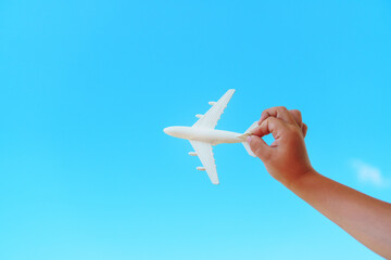 A white toy plane in a child's hand against a blue sky.