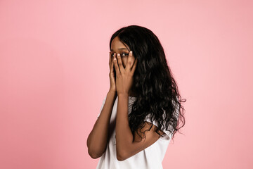 Scared. Cheerful african-american young woman isolated on pink background, emotional and expressive. Concept of human emotions, facial expression, sales, ad. Beautiful model with long curly hair.