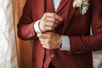 Closeup of a groom in maroon suit correcting a sleeve.