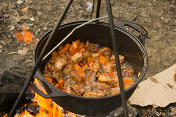 Cooking camping outdoor meal in an open fire in a travel pot with blaze. Dinner during travel.