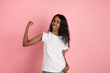 Strong, power. Cheerful african-american young woman isolated on pink background, emotional and expressive. Concept of human emotions, facial expression, sales, ad. Beautiful model with long curly