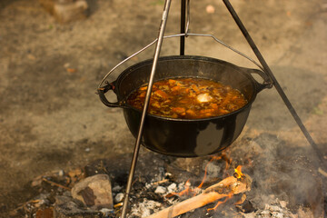 Cooking camping outdoor meal in an open fire in a travel pot with blaze. Dinner during travel.
