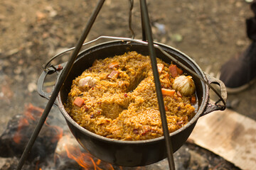 Cooking camping outdoor meal in an open fire in a travel pot with blaze. Dinner during travel.