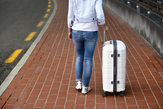 The girl holds the handle of a white suitcase at the airport.Vacation, tourism and travel concept - young woman tourist walking with suitcase in airport or station.