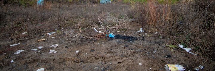 Paper and plastic garbage on brown clay near dry bushes. Sample of pollution environment by humans activities. Landscape image with nature background and copy space.