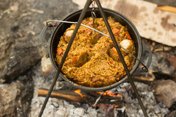 Cooking camping outdoor meal in an open fire in a travel pot with blaze. Dinner during travel.