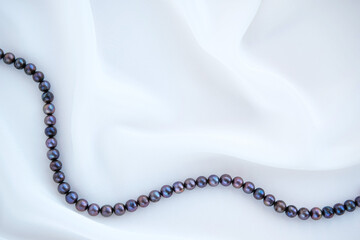 Elegant white silk background with black pearls necklace.