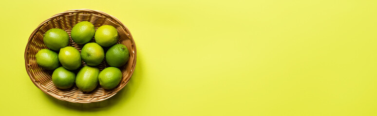 top view of ripe limes in wicker basket on colorful background, panoramic crop