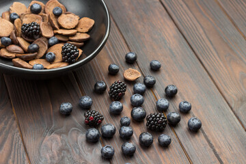 Blueberries and blackberries on table. Chocolate pancakes and berries in black ceramic bowl.