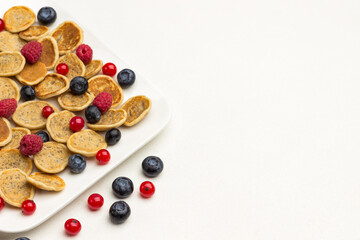 Mini pancakes and berries in plate. Red currants, blueberries  on white background