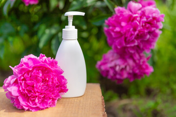 white cosmetic bottle for soap or shampoo on wooden shelf with peonies background. For montage of your product