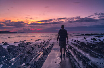 Fototapeta premium A young man by the sea at Sakoneta Beach and his beautiful Flysch in the town of Deba, At the western end of the Geopark of the Basque Coast, Guipúzcoa. Basque Country
