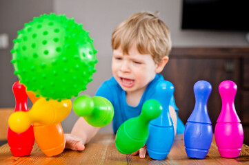 Obraz premium Children a boy throws ball into a home bowling alley and smashes the bowling pins. Selective focus. concept of active play in the home room, quarantine, self-isolation, achieving goal.