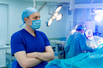 Doctor stands cross hands. Blue scrubs. Robotic medical equipment background.