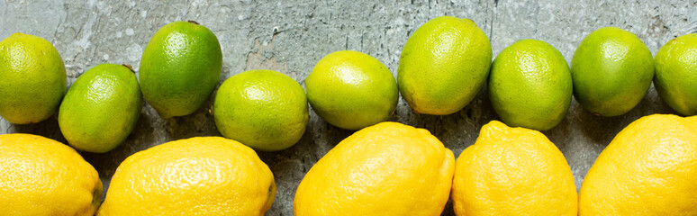 top view of ripe yellow lemons and green limes on concrete textured surface, panoramic crop