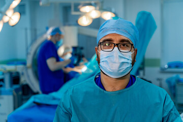 Fototapeta na wymiar Head and shoulders portrait of male doctor wearing protective mask and looking at camera posing against operating room background. Copy space