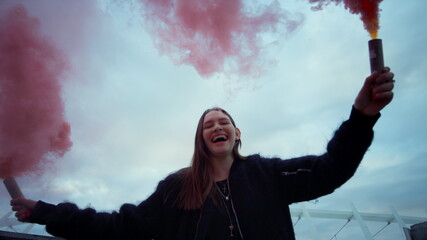 Girl moving smoke bombs in hands. Woman posing on street in colorful smoke