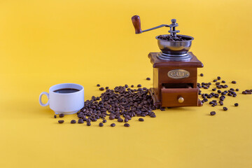 vintage manual coffee grinder with coffee beans and a Cup on a yellow background