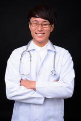 Young handsome Asian man doctor against black background