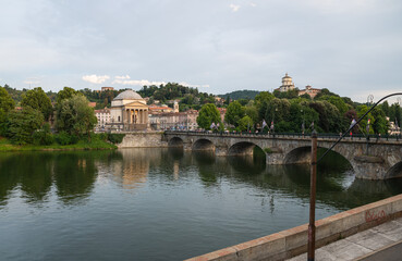 Fototapeta na wymiar Turin, Piedmont, Italy. July 2020. Wonderful evening view of the Gran Madre church overlooking the Po river. The waterfall downstream of the dam is highlighted. On the bridge people and cars.