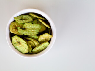 Green color banana chips with hot green chili flavor in a white bowl against white background,  with copy space