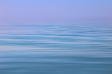 Naklejka premium Calm sea wavy surface of the sea under a clear sky close-up. Blue and purple background.