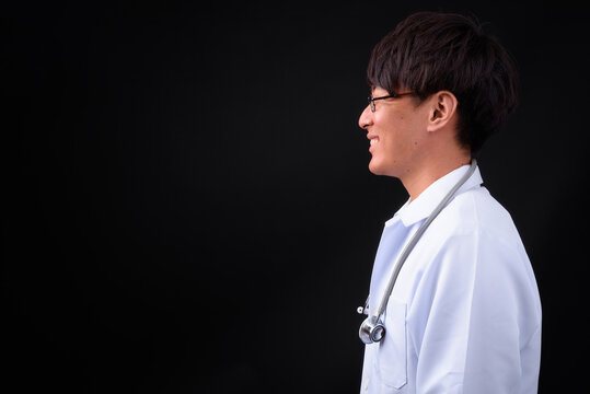 Young handsome Asian man doctor against black background