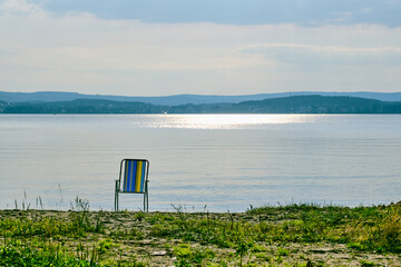 Deck chair standing alone on the shore of the lake.