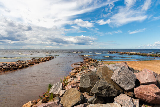 Stone Breakwater Going Into The Sea. The Transition Of A Rainy Sky To A Clear Blue With White Clouds.