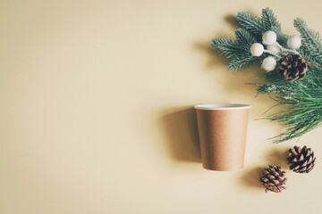 Brown disposable paper cup of coffee, green fir branch and cones on a beige background. Merry Christmas and Happy New Year wallpaper and mockup
