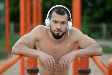 Obraz premium A man with headphones rests after doing push UPS on the bars outside