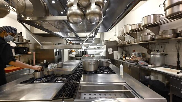 Team of professional chefs preparing and cooking food in a commercial kitchen. Zoom out, Dolly shot camera movement. High quality 4k footage
