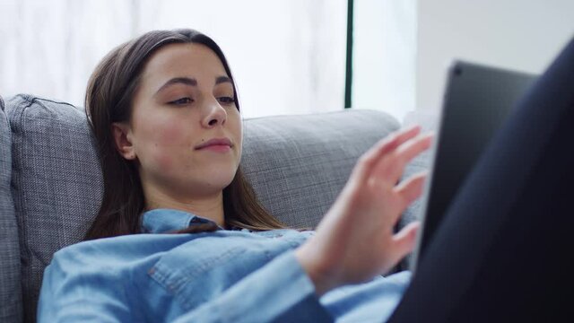 Relaxed young woman at home lying on sofa looking at digital tablet - shot in slow motion