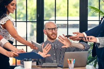 Too many work. Selective focus of young business man surrounded by colleagues, each proposes a...