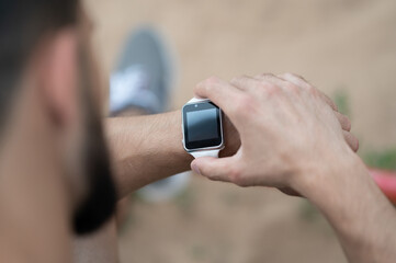 Close up of man using smart watch on street. Portrait of athletic male with fitness tracker in hand. Healthy lifestyle