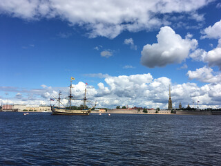 Fototapeta na wymiar View of the Neva river, the Peter and Paul fortress and the sailing ship Poltava, which arrived to participate in the naval parade in St. Petersburg against a blue sky with clouds...