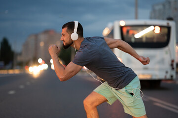 An adult athlete jogs through the city at night, a man runs across a pedestrian crossing