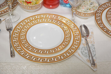 Empty plate , gold set on wooden white table . Beautifully decorated table with gold plates, linen napkin , spoon, fork .