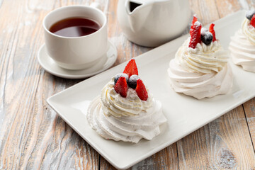 Three small portions of anna pavlova meringue dessert, topped with blueberry and strawberry on wooden table, close up