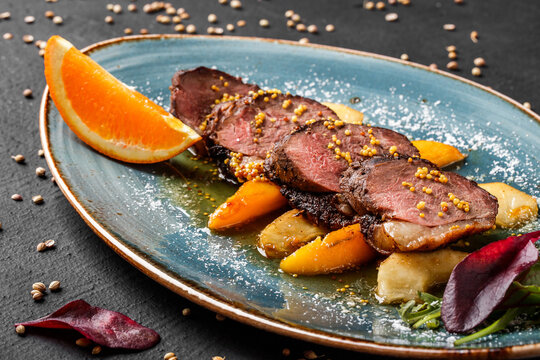 Juicy duck breast steaks with caramelized fruit, mango, apple and sauce of orange on plate over dark stone background. Hot Meat Dishes